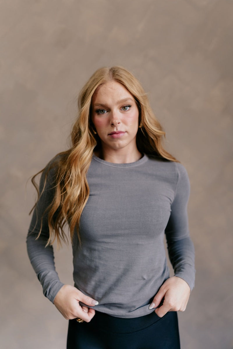 Front view of model wearing the Lea Charcoal Basic Long Sleeve Top that has charcoal grey knit fabric, a round neckline, and long sleeves.