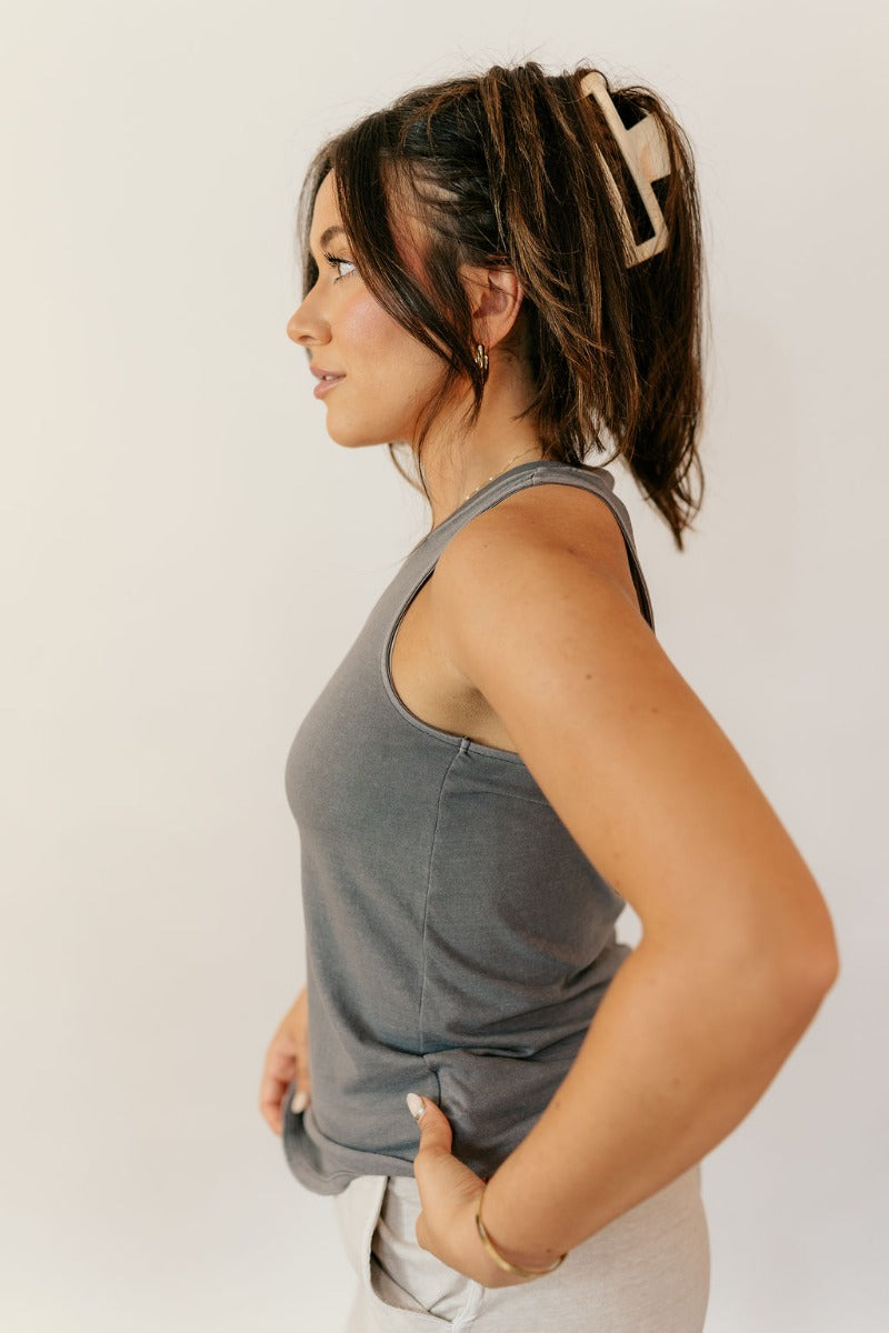 Side view of model wearing the Hadley Charcoal V-Neck Pocket Tank that has charcoal grey knit fabric, a scooped hem, a front right chest pocket with raw hem, a v-neck, and a racerback design.
