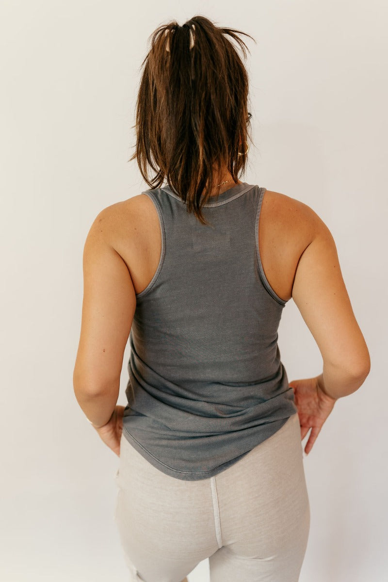Back view of model wearing the Hadley Charcoal V-Neck Pocket Tank that has charcoal grey knit fabric, a scooped hem, a front right chest pocket with raw hem, a v-neck, and a racerback design.