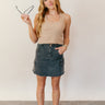 Full body front view of model wearing the Kimber Black Denim Mini Skirt that has black washed denim fabric, mini length, a fray hem, pockets, a front zipper with a button closure, belt loops, and two back pockets.