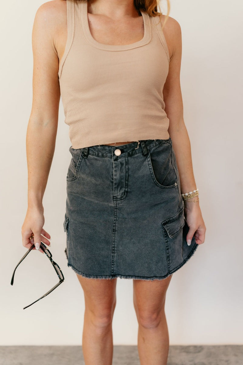 Front view of model wearing the Kimber Black Denim Mini Skirt that has black washed denim fabric, mini length, a fray hem, pockets, a front zipper with a button closure, belt loops, and two back pockets.