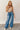 Full body front view of model wearing the Ceros: Billie Wide Leg Paper Bag Jeans that have medium wash denim fabric, pockets, a front zipper, belt loops, an elastic paperbag waist, and wide legs with raw hems.