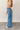 Full body side view of model wearing the Ceros: Billie Wide Leg Paper Bag Jeans that have medium wash denim fabric, pockets, a front zipper, belt loops, an elastic paperbag waist, and wide legs with raw hems.