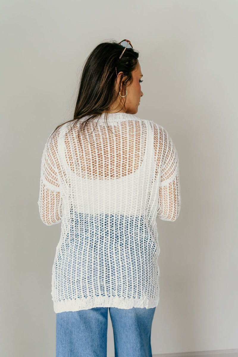 Back view of model wearing the Remington Ivory Crochet Knit Cardigan that has ivory open knit fabric, a front opening with no closure, a thick hem, two front pockets, and long sleeves.