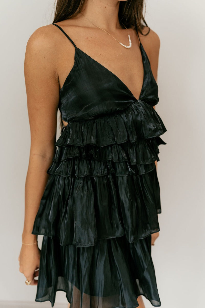 Close up view of model wearing the Everly Black Ruffle Tiered Sleeveless Mini Dress which features black sheer fabric, two tiered style, ruffle details, black lining, a plunge neckline, adjustable straps, and an open back with a tie closure.
