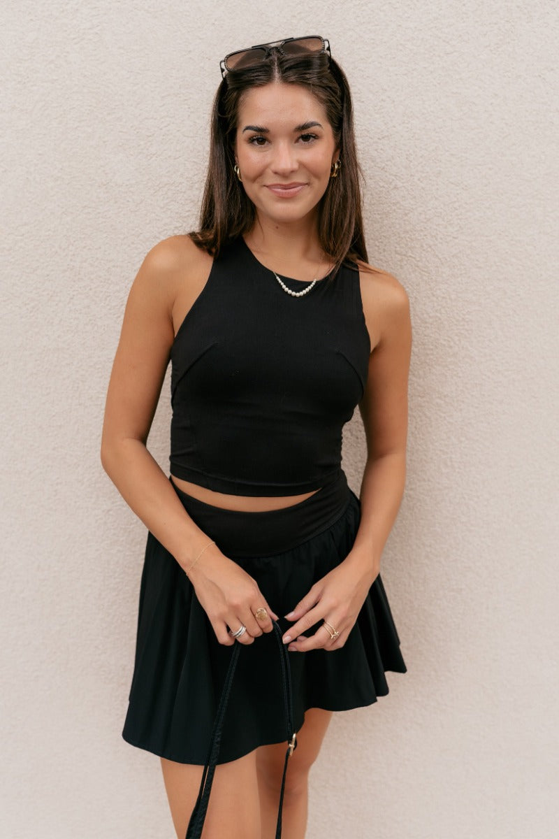 front view of model wearing the Carter Black Racerback Cropped Tank Top that has black athleisure fabric, a cropped waist, built-in padding, and a round neckline with a racerback.