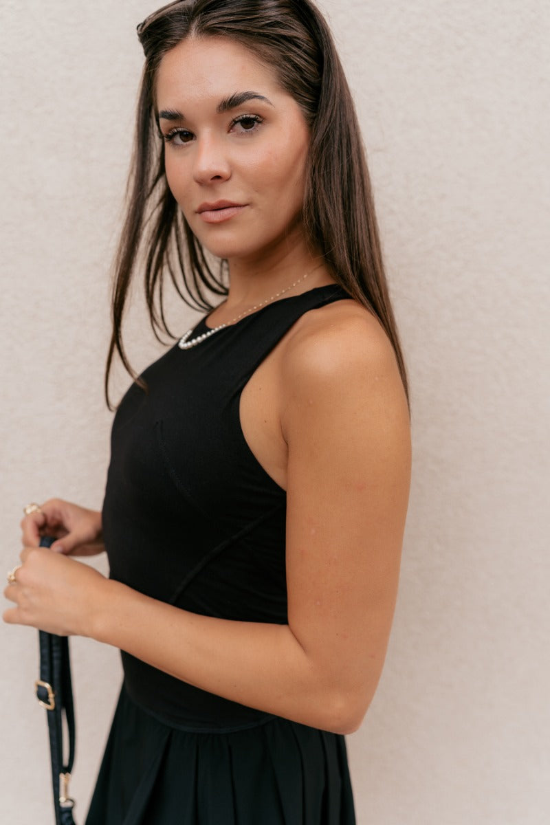 Close side view of model wearing the Carter Black Racerback Cropped Tank Top that has black athleisure fabric, a cropped waist, built-in padding, and a round neckline with a racerback.