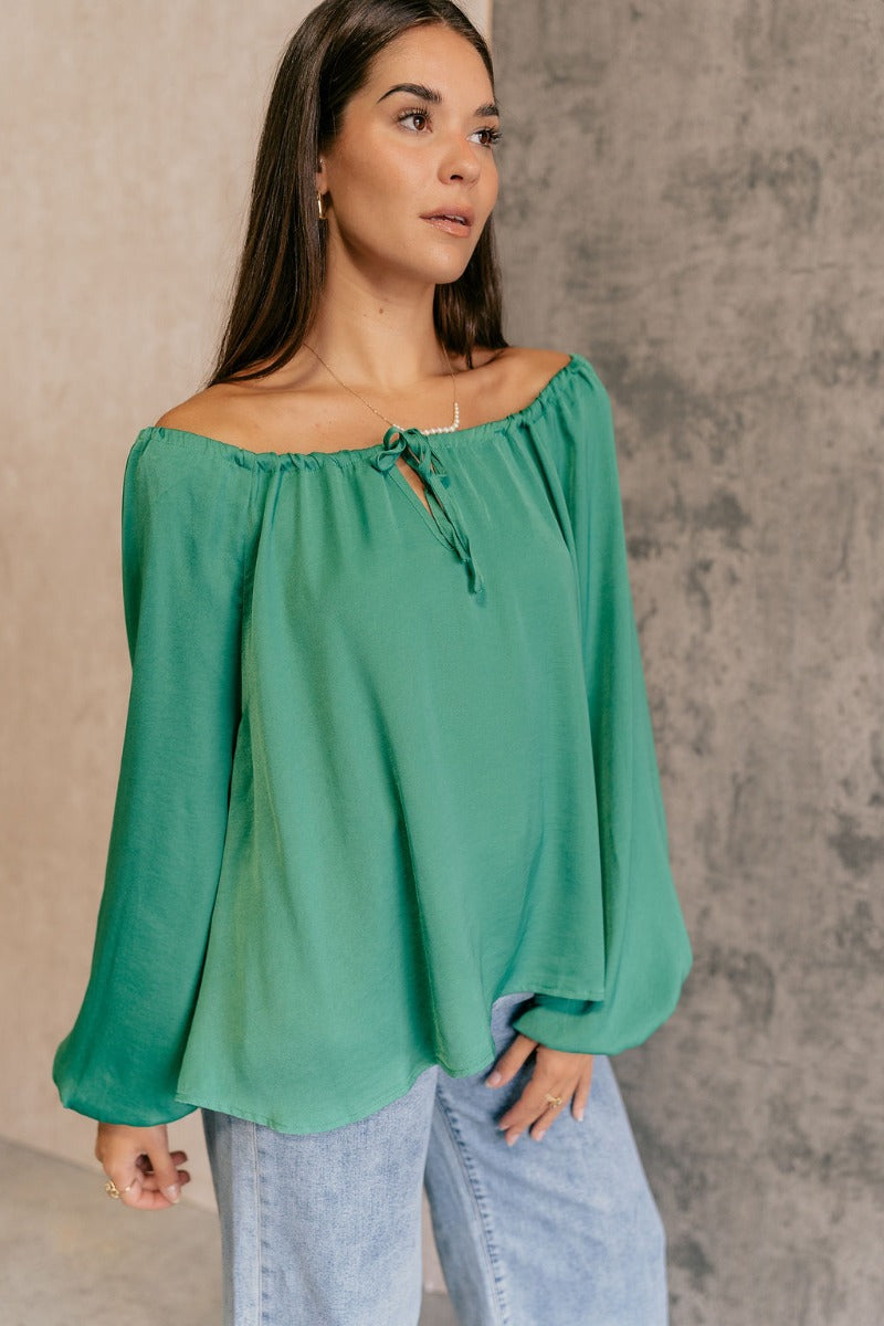 Front side view of model wearing the Audrey Green Satin Adjustable Neckline Long Sleeve Top which features green satin fabric, a round neckline with a drawstring tie, and long balloon sleeves with elastic wrists.
