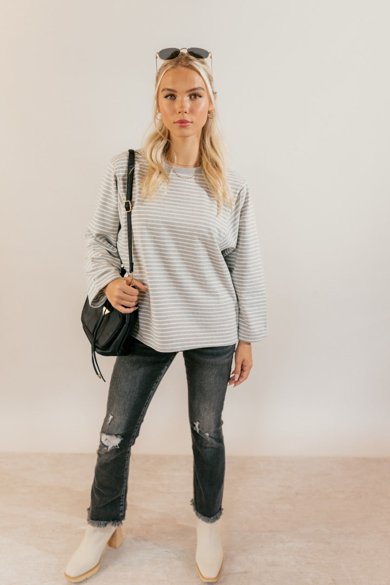 Full body untucked view of model wearing the Samantha Grey & White Striped Long Sleeve Top that has grey and white knit fabric, stripe pattern, slits, a round neck, and long flare sleeves.