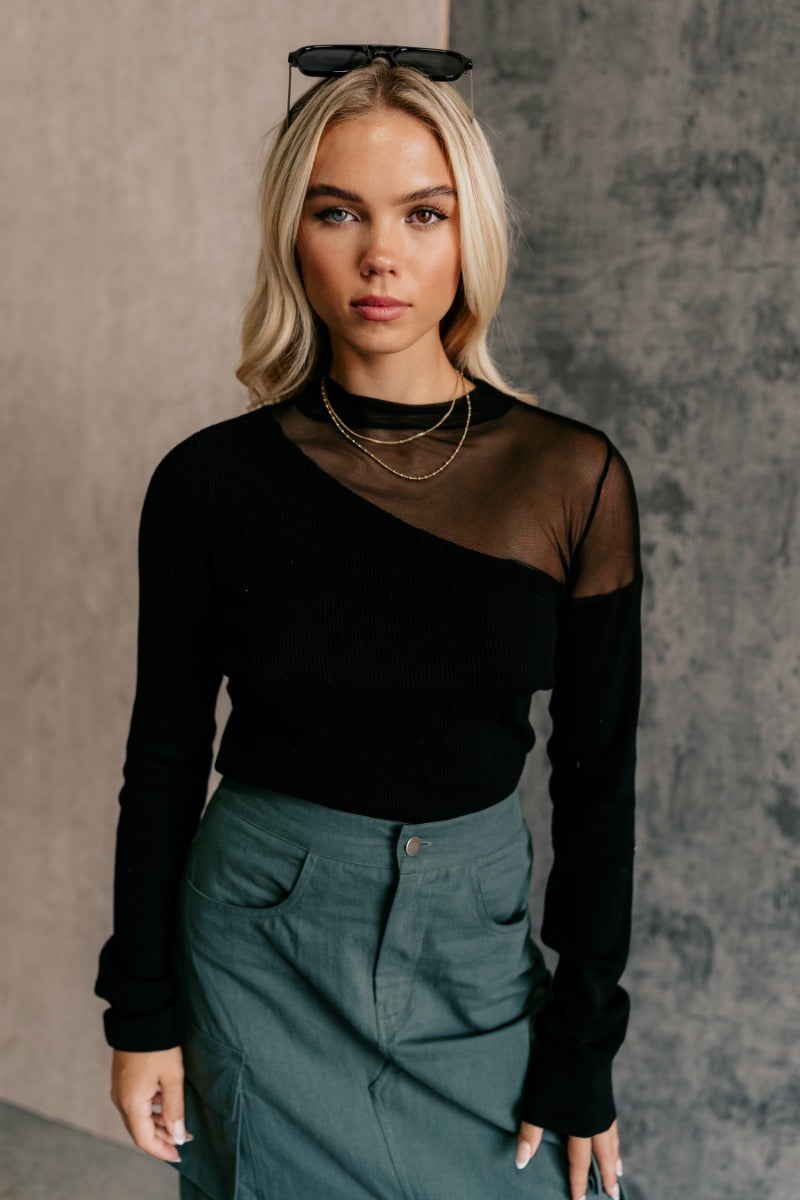 front view of model wearing the Callie Black Mesh Detail Long Sleeve Top that features black ribbed knit and black mesh fabric, a high neckline, and long sleeves.