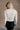 back view of model wearing the Norah Off White Mock Neck Top that has off white ribbed fabric, a high neckline, and long sleeves.