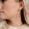 Side view of model wearing the Luna Purple Beaded Gold Fringe Earring which features gold chain fringe dangle earrings with grey and taupe beading.