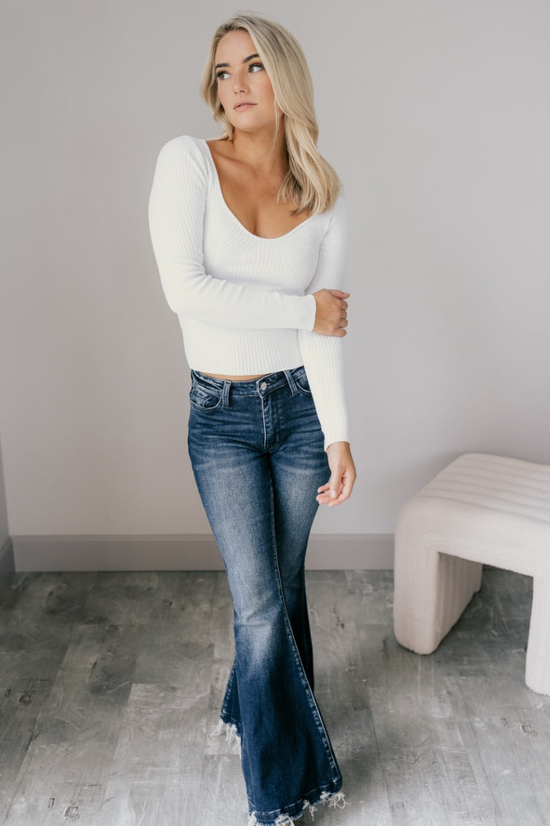 Full body view of model wearing the Rooted Denim: Leah Dark Wash Flare Leg Jeans which features dark wash denim fabric, a front zipper with a button closure, two front pockets, two back pockets, belt loops, and flared legs with fray hem.