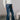 Full body side view of model wearing the Rooted Denim: Leah Dark Wash Flare Leg Jeans which features dark wash denim fabric, a front zipper with a button closure, two front pockets, two back pockets, belt loops, and flared legs with fray hem.