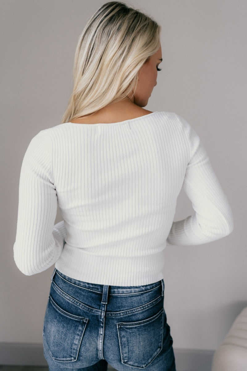 Back view of model wearing the Ember Off White Long Sleeve Ribbed Top which features off white ribbed fabric, a sweetheart neckline, and long sleeves.