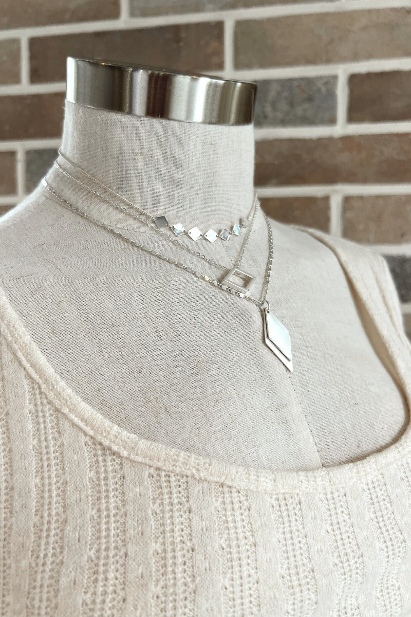 The Time To Travel Necklace In Silver features matte silver triple layer chain link and short length chain with diamond shaped attachments.