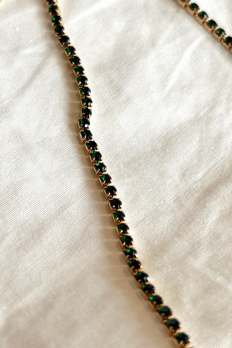 Close up view of the Beyond The Pines Necklace which features green stones set in gold.