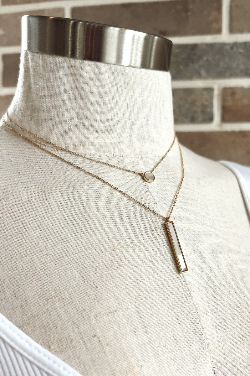 Full view of the Dream Big Necklace which features a double chain with two cream stones, one shaped as a circle and the other shaped as a rectangle.