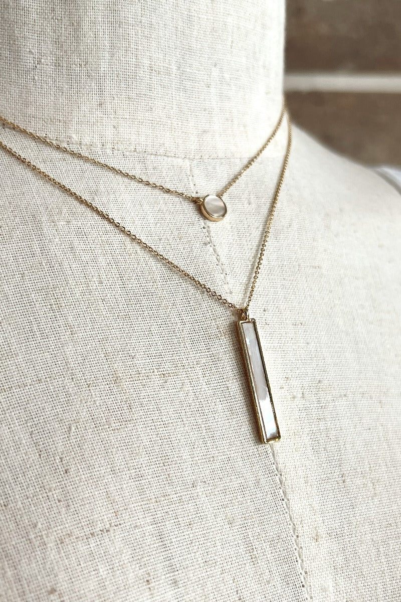 Close up view of the Dream Big Necklace which features a double chain with two cream stones, one shaped as a circle and the other shaped as a rectangle.