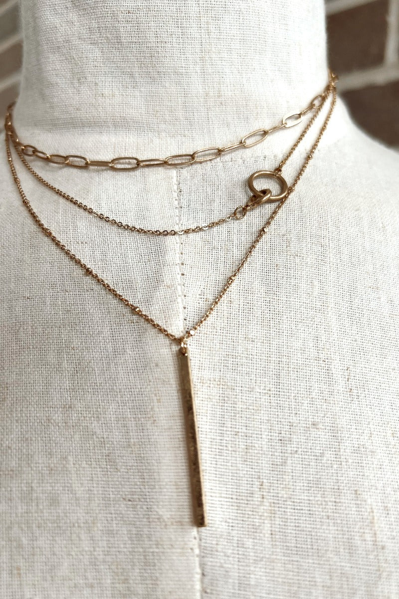 Close up view of the Raise The Bar Necklace in Gold which features triple layer chain link, larger chain link and gold bar at the end.