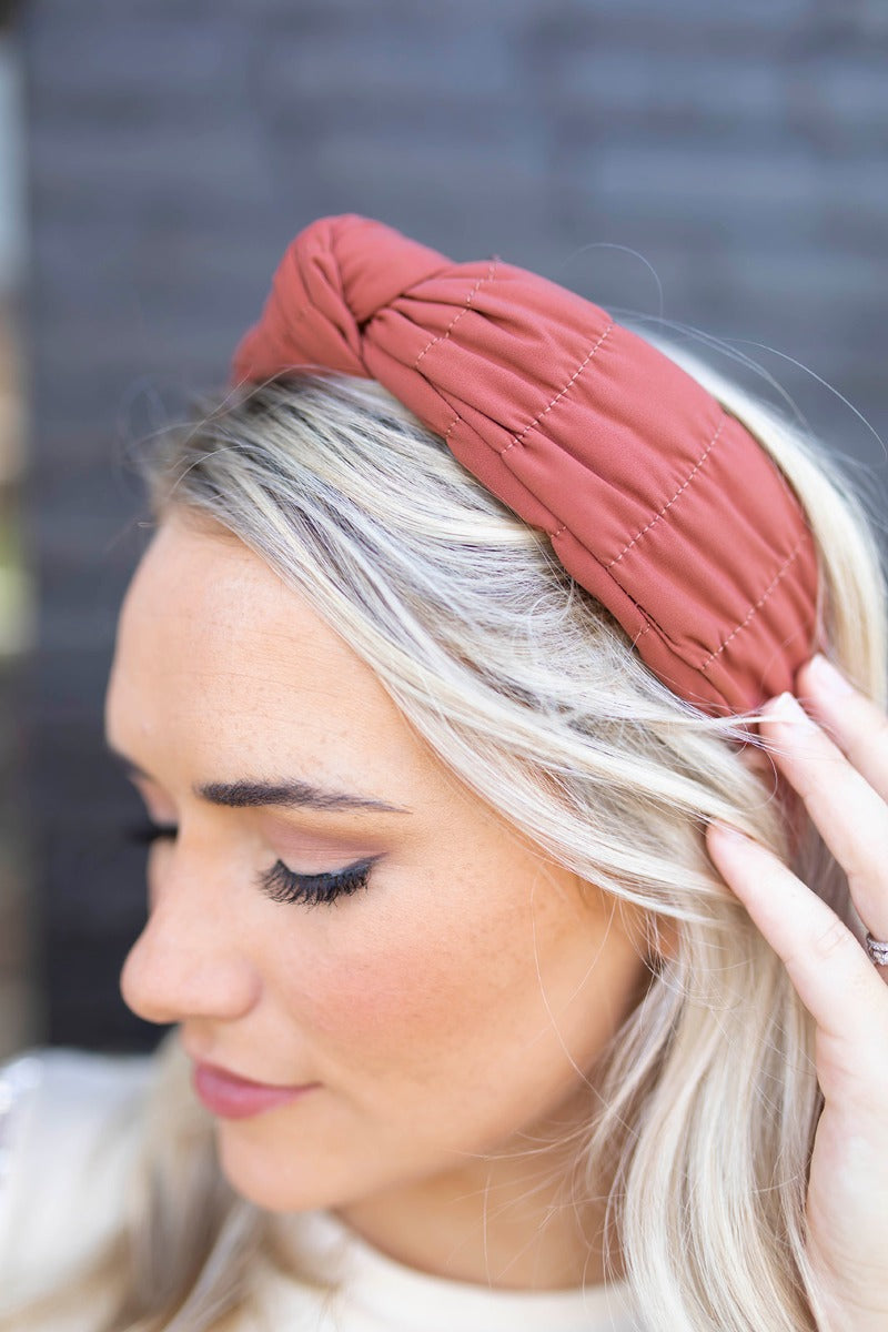 Close side view of model wearing the Sadie Headband in Rust, which features a structured band with a satin lining and a quilted exterior with a top twist.