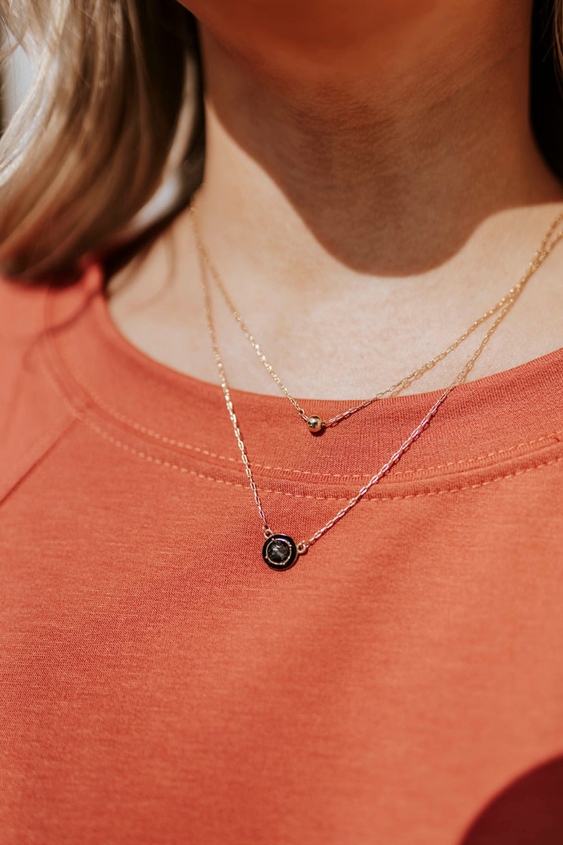 Close up view of model wearing the Ultimate Jewel Necklace which features double layer gold chain with black circle stone and gold circle medallion.
