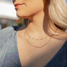 Close up view of model wearing the Emerald Views Necklace which features a double layer gold chain with green stones. 