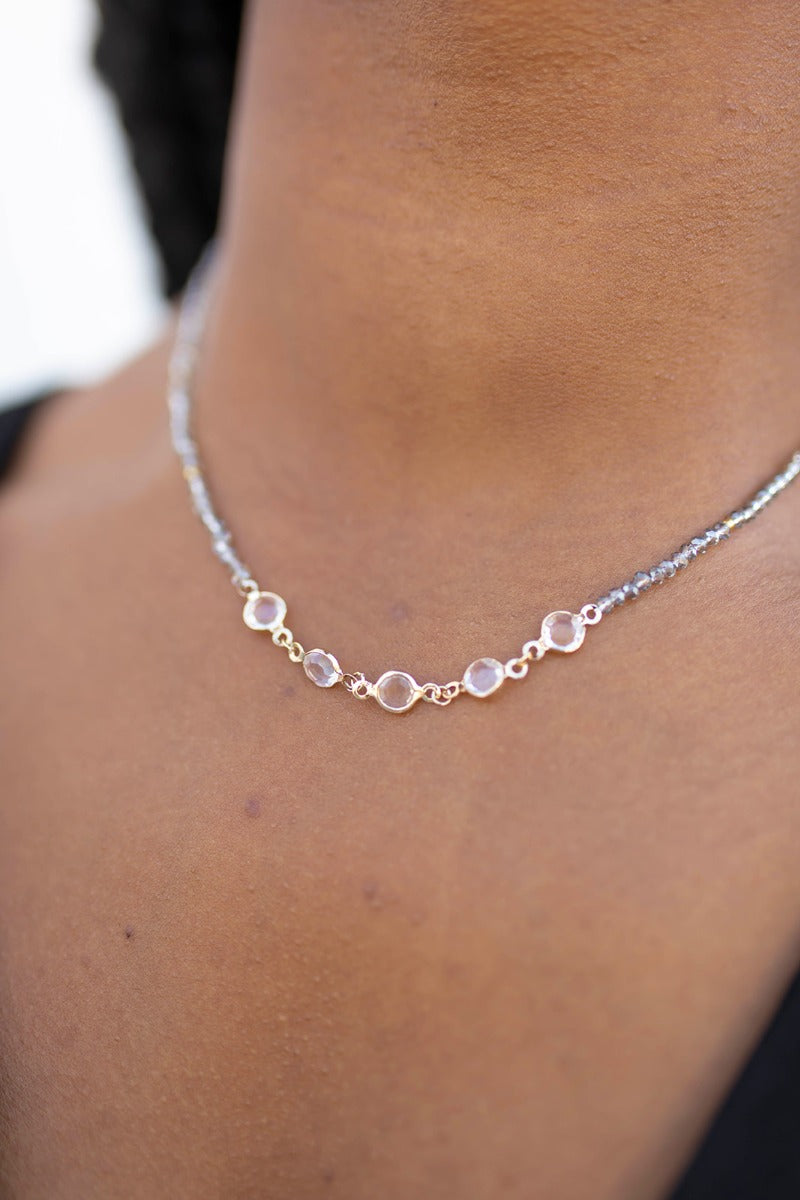 Close up view of model wearing the Good Reputation Necklace which features one layer covered with grey beads and 5 clear stones.