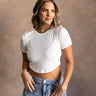 Front view of model wearing the Gabrielle White Short Sleeve Crop Top that have white ribbed knit fabric, a cropped waist, a round neckline and short sleeves.