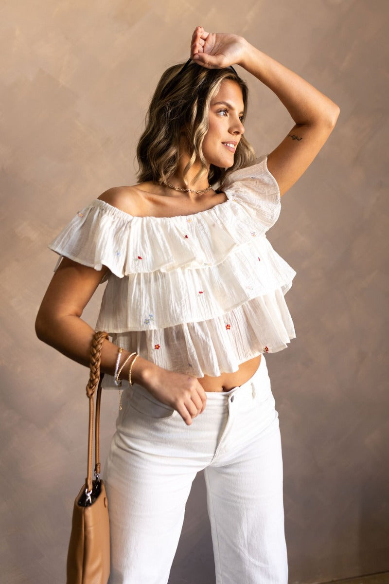 front view of model wearing the Carolina Ivory Tiered Floral Top that has ivory light weight fabric, a three tiered design, multi color embroidered flower details, a square neckline and ruffle straps.