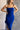 CLose up view of model wearing the Liliana Blue Asymmetrical Sleeveless Midi Dress which features royal blue knit fabric, an asymetrical ruffle hem, midi length, a square neckline, and adjustable straps.