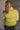 Back view of model wearing the Mckenna Chartreuse Puffer Vest that has yellow-green puffer fabric, a zip-up front with a high neckline, and front slit pockets.