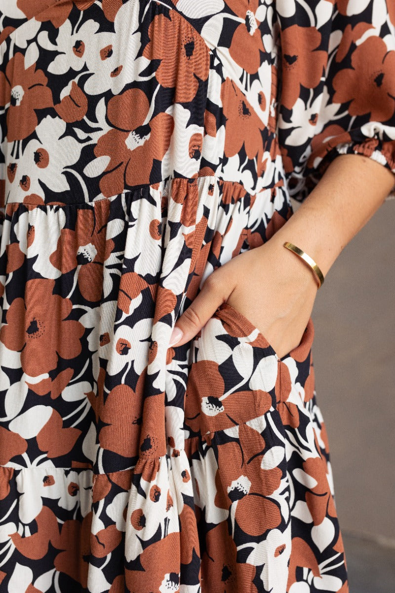 Close-up pocket view of model wearing the Selah Black & Brown Floral Mini Dress that has a black, brown and white floral print, a flare skirt,a scooped neckline, short puff sleeves, and a smocked back.