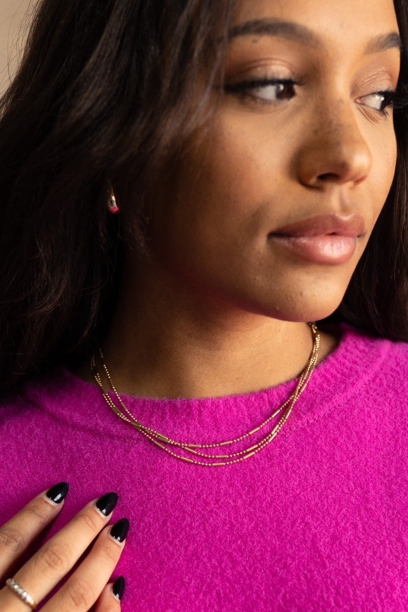 Front view of model wearing the Valentina Gold Layered Necklace that has three gold layers with gold beads and gold bar design.