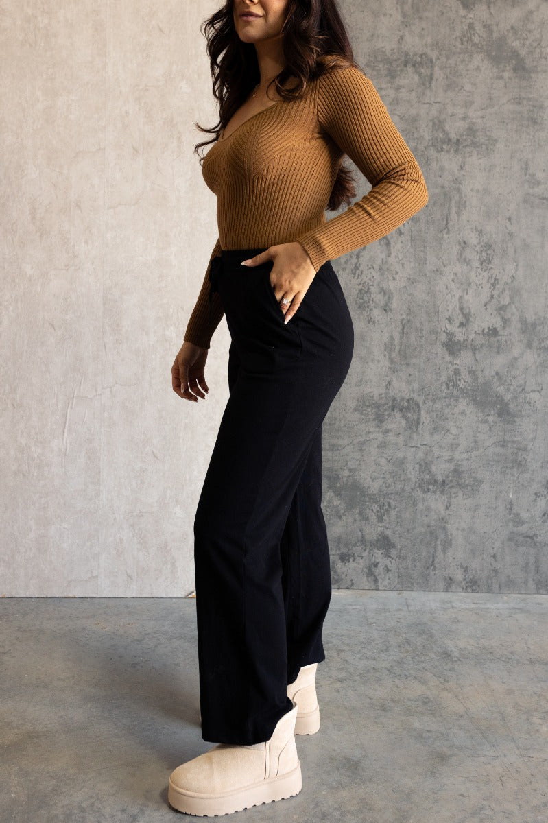Full body side view of model wearing the Aubrey Black Lounge Pants which features black cotton fabric, two front pockets, an elastic waistband with drawstring ties, and wide legs.