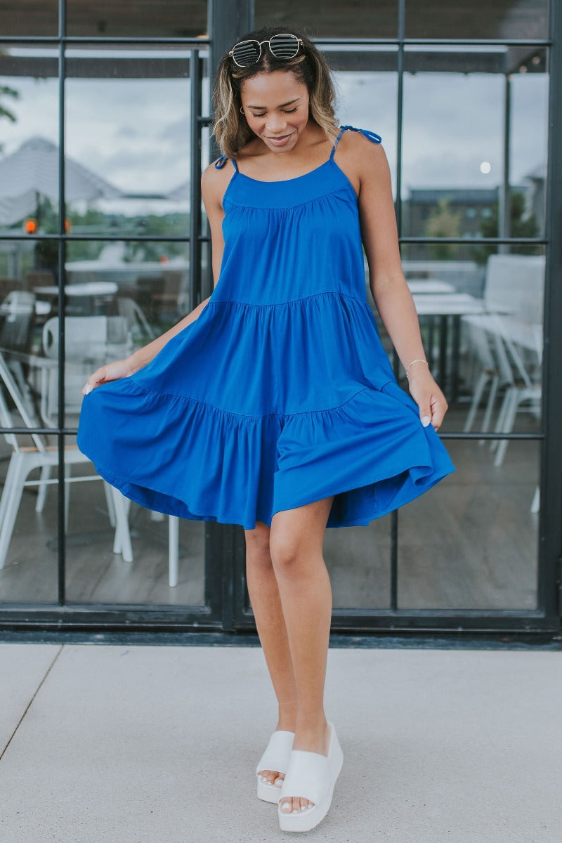 Full body front view of model wearing the Summer Shade Romper that has cobalt blue fabric, a two-tiered body, a scooped neckline, and tie straps.