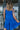 Back view of model wearing the Summer Shade Romper that has cobalt blue fabric, a two-tiered body, a scooped neckline, and tie straps.