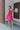 Full body back view of model wearing the Sweet Energy Mini Dress which features hot pink fabric, a mini hem length, a three-tiered body, hot pink lining, a v-neckline, and ruffle straps.