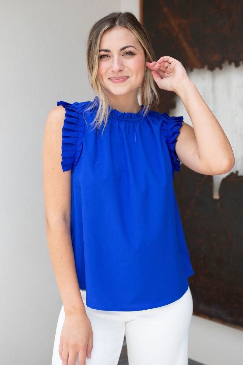 Front view of model wearing the Buena Vista Ruffle Tank that has royal blue fabric, a high neck with ruffle details, and a sleeveless design with pleated ruffle details
