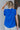 Back view of model wearing the Buena Vista Ruffle Tank that has royal blue fabric, a high neck with ruffle details, and a sleeveless design with pleated ruffle details