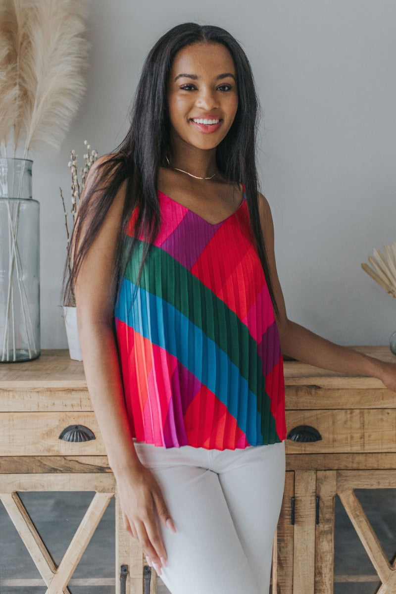 Front view of model wearing the Stuck On You Tank which features red, orange, pink, blue, green and purple pleated fabric, stripe pattern, orange lining, v-neckline, adjustable straps and sleeveless.