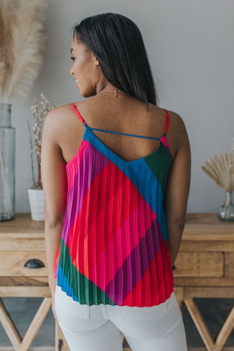Back view of model wearing the Stuck On You Tank which features red, orange, pink, blue, green and purple pleated fabric, stripe pattern, orange lining, v-neckline, adjustable straps and sleeveless.