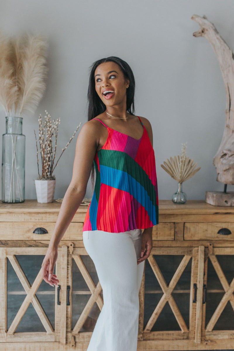 Side view of model wearing the Stuck On You Tank which features red, orange, pink, blue, green and purple pleated fabric, stripe pattern, orange lining, v-neckline, adjustable straps and sleeveless.