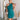 Frontal view of the Tell Me About It Dress that features a teal ribbed material, a high round neckline, a sleeveless design with one shoulder thick strap, a tight fit, and a mini length.