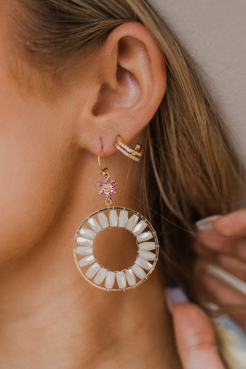 Close up image of model wearing The Follow The Flowers Earring, which features a pink rhinestone flower and a gold circle pendant with beige beading.