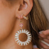 Close up image of model wearing The Follow The Flowers Earring, which features a pink rhinestone flower and a gold circle pendant with beige beading.