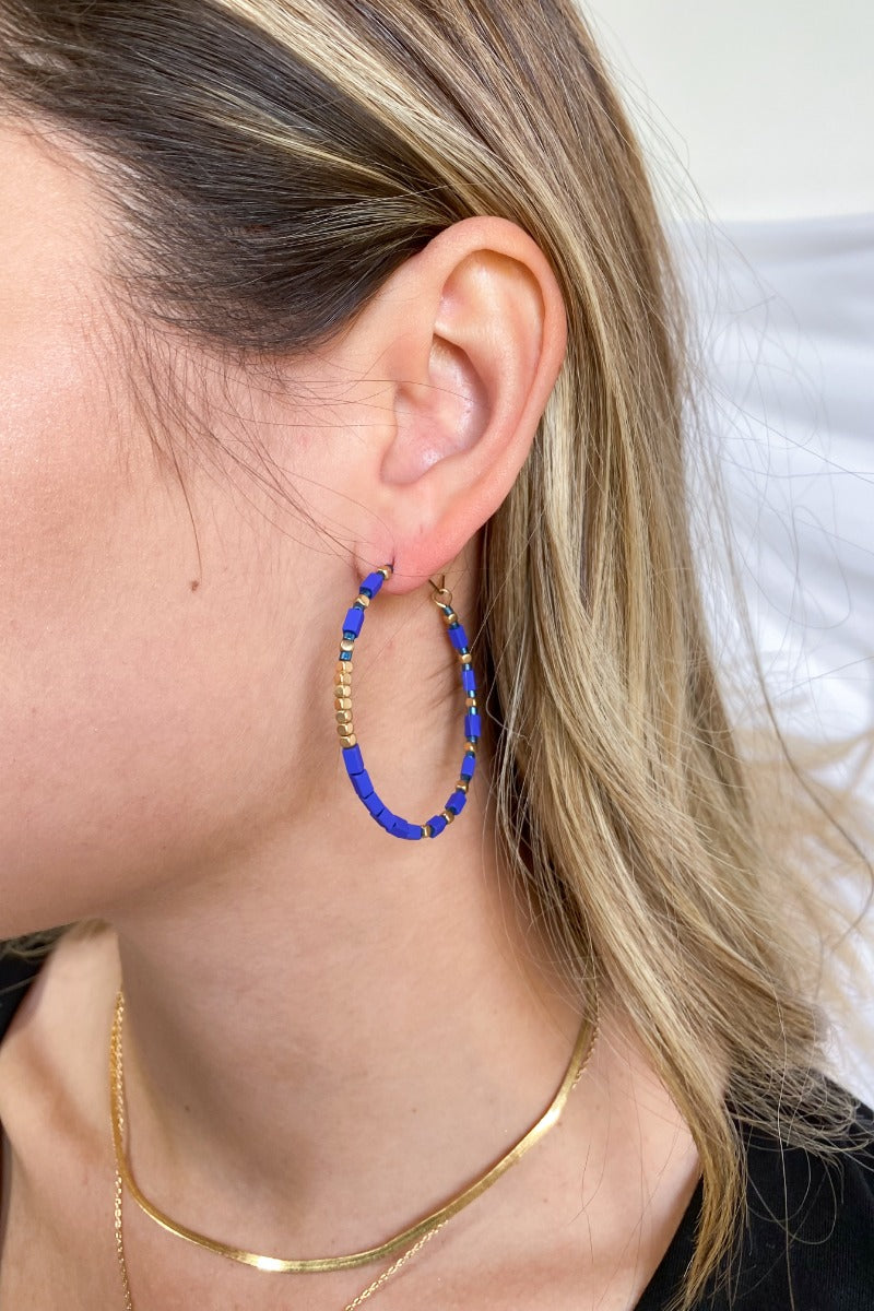 Close up view of the Winter Skies Earrings features gold hoop filled with blue and gold beads. 