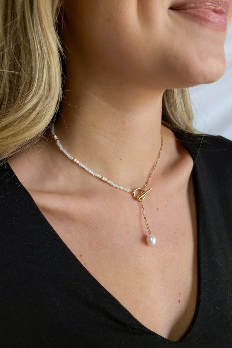 Close up view of model wearing the Mother Of Pearl Necklace features gold chain link with white beads linked with a gold circle lariat and pearl.