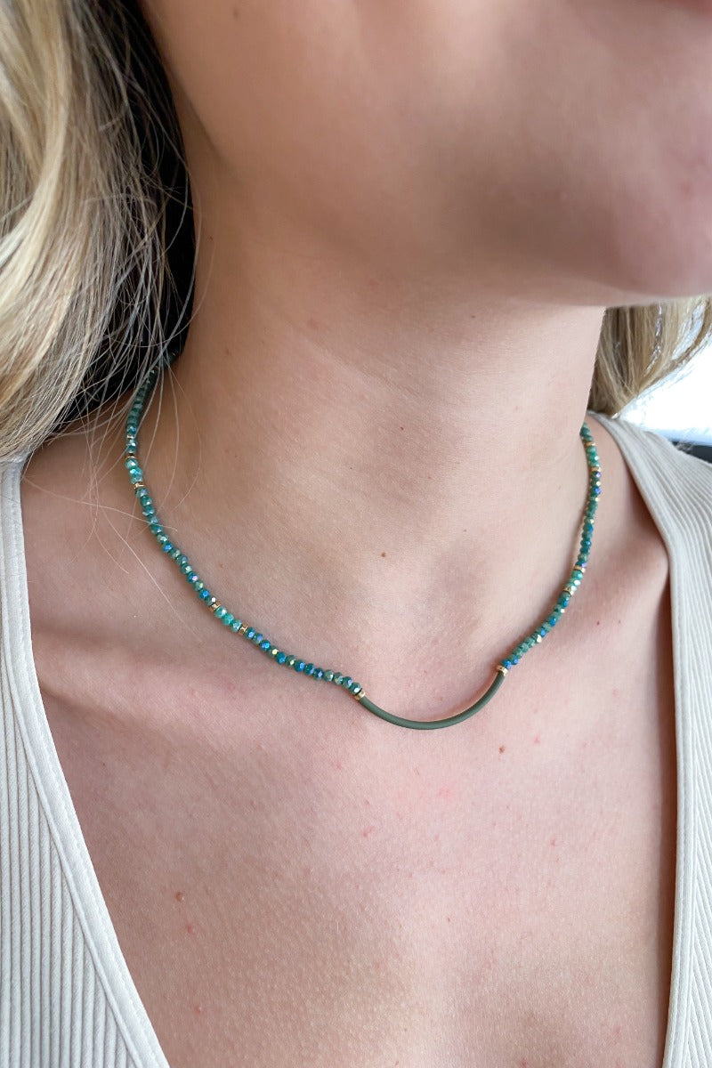 Close up view of model wearing the Forest Views Necklace which features green and aqua color beads linked with a green swooped link.