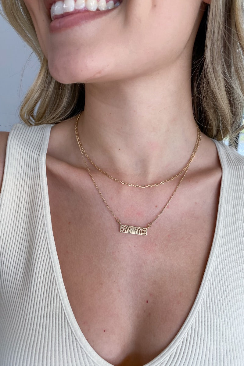 Close up view of model wearing the Take A Walk Necklace in Gold features gold double chain layer with a rectangle design medallion.